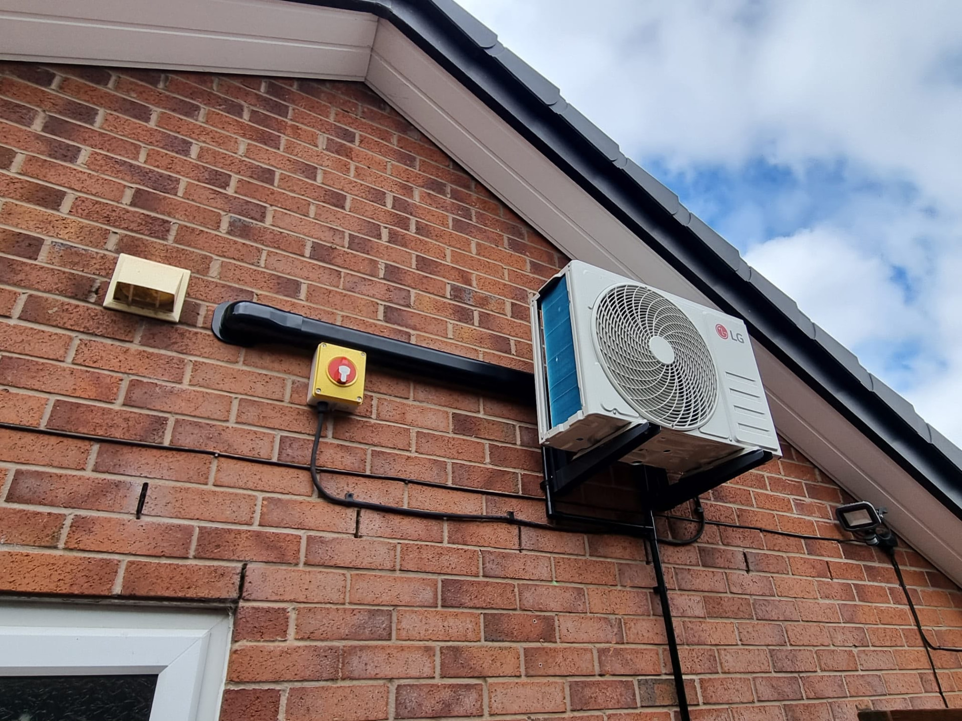 LG external air conditioning condenser mounted high on the brick gable wall of a house
