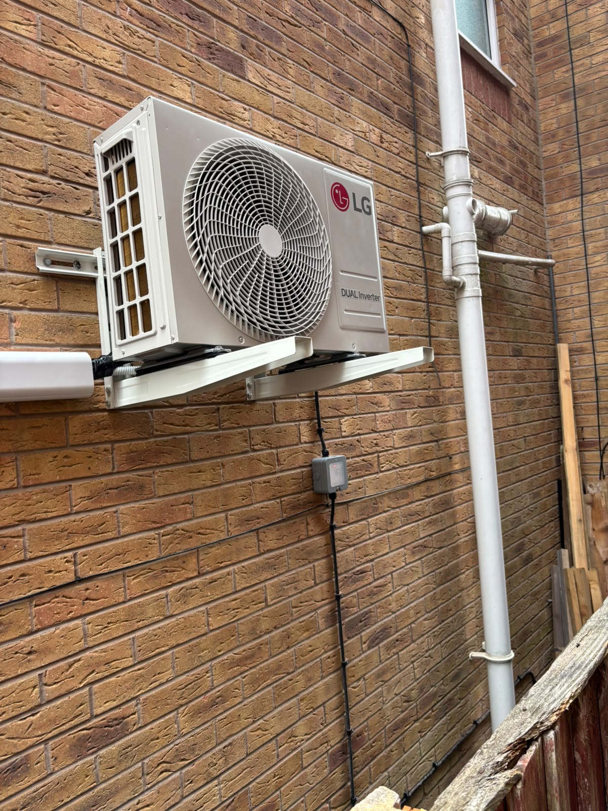 LG DUAL Inverter external condenser unit mounted on brackets against a brick wall
